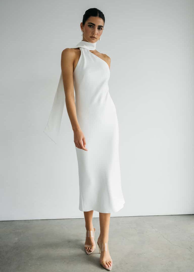 Woman wearing a white halter neck dress against a plain background