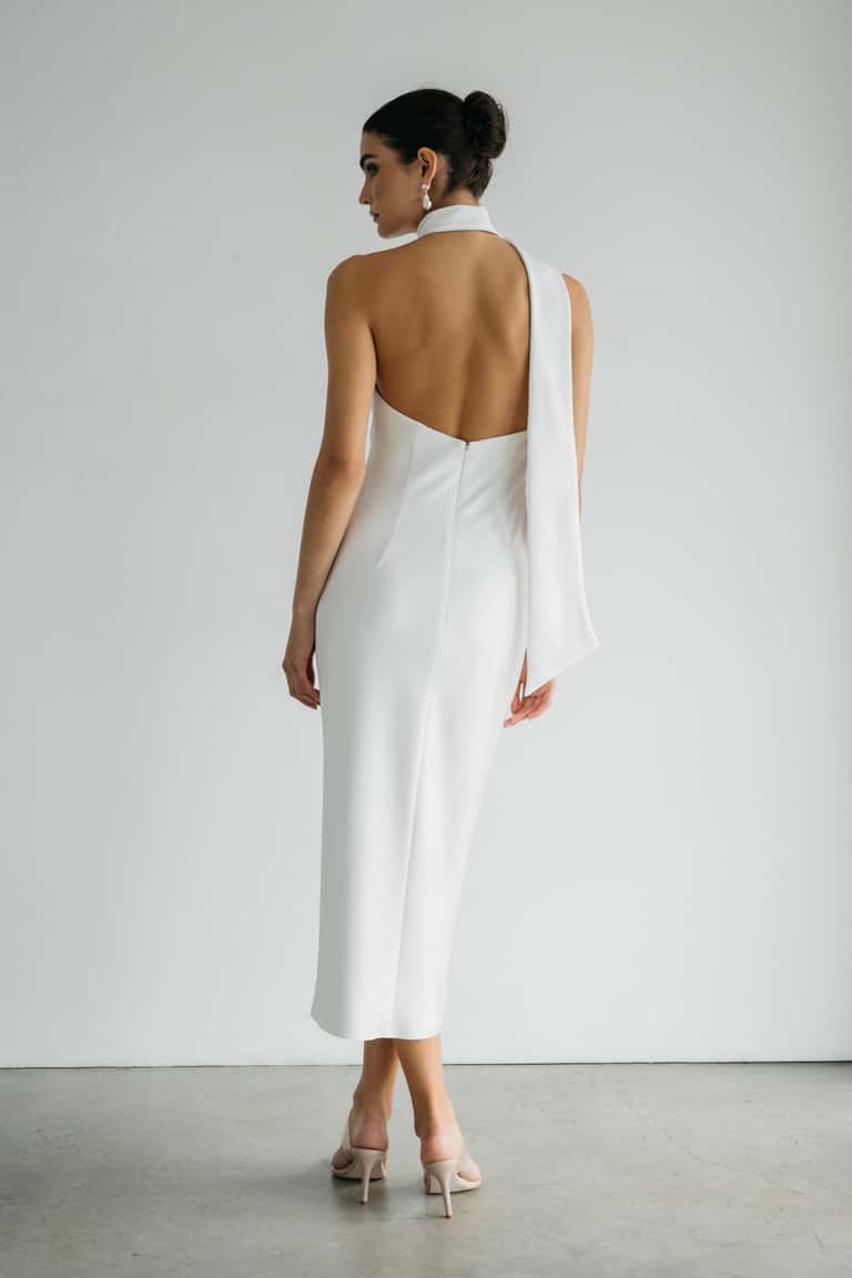 Woman wearing a white dress with a high slit and long sleeves against a plain background