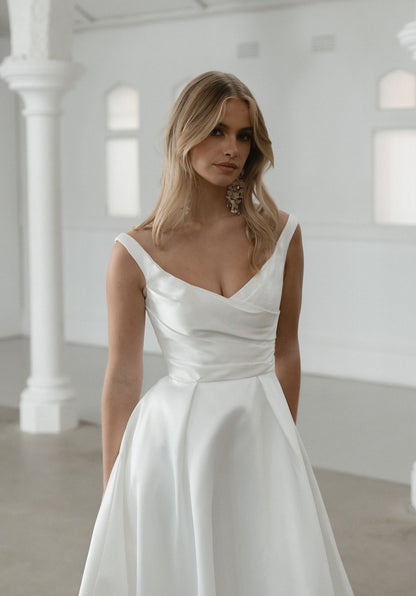 Seldon captures the essence of simple elegance, showcasing a pleated bodice that gracefully complements her shallow V neckline and signature Mikado fabric.