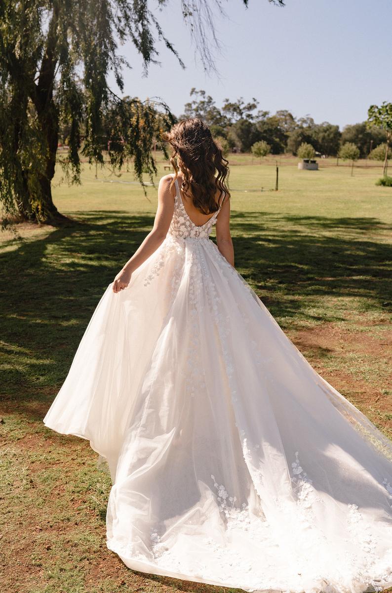 Woman in a white wedding dress standing in a park with trees and grass.