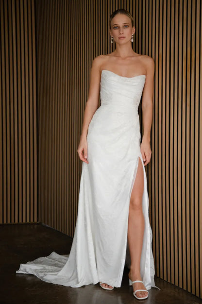 Woman wearing a strapless white wedding dress with a slit on a wooden paneled background