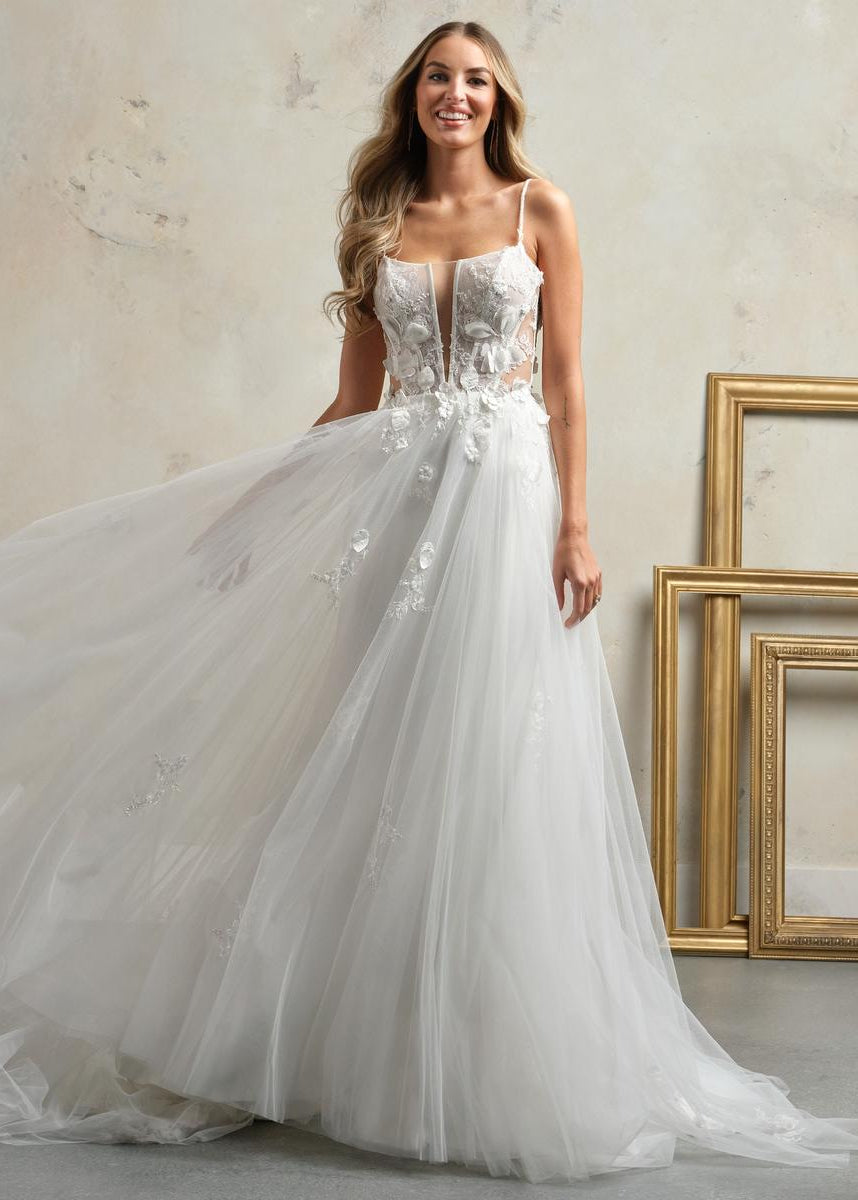 Woman wearing a white wedding dress with floral details in a studio setting.