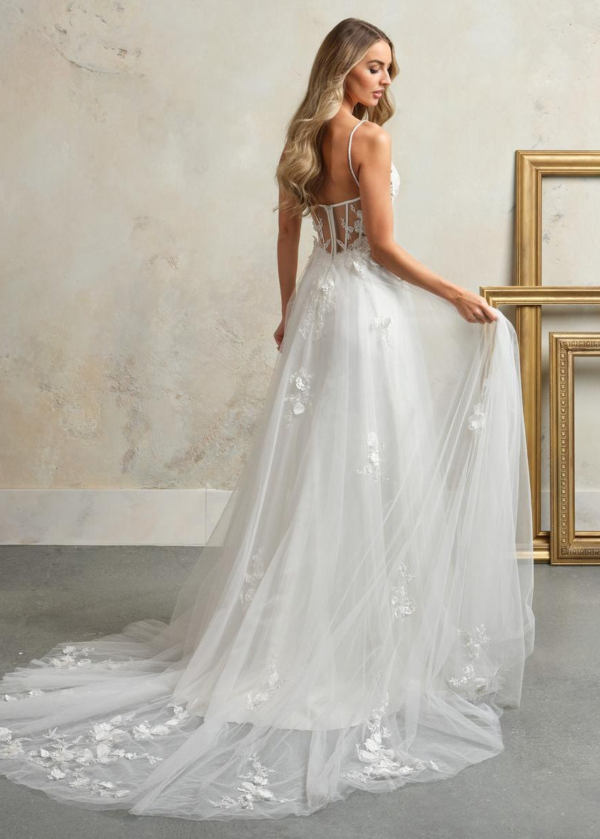 Woman in a white wedding dress with floral details in a room with gold frames.