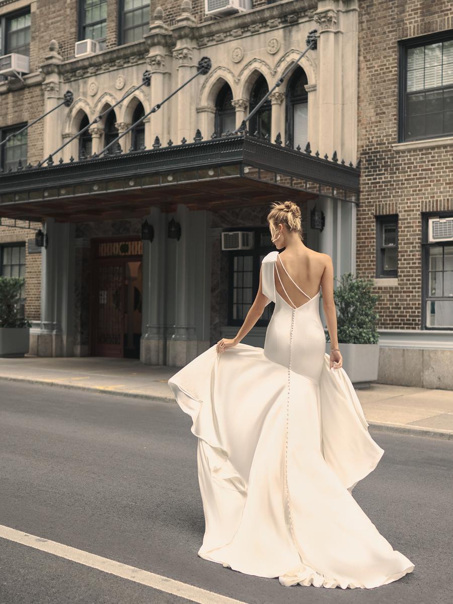 Woman in a white wedding dress standing on a city street with an elegant building in the background