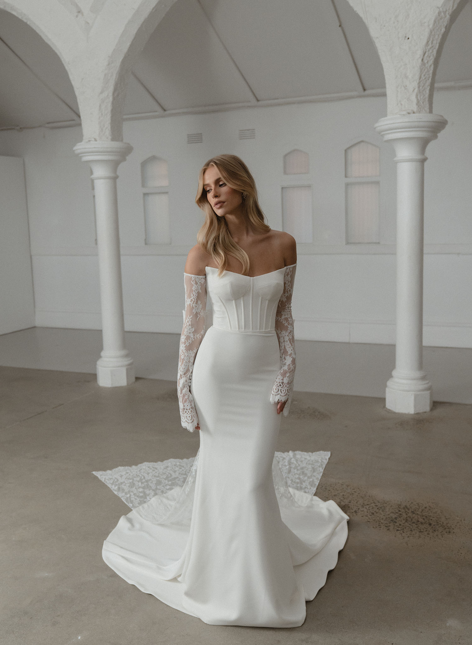 Woman in a white wedding dress standing in a spacious room with arched columns.