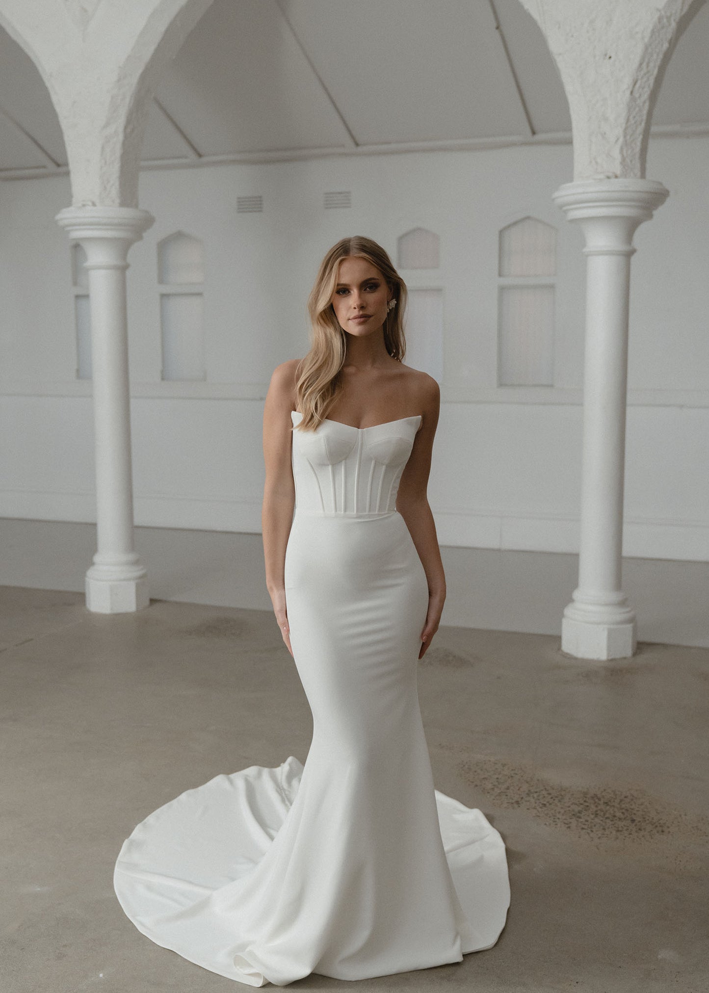 Woman in a white strapless gown standing in an elegant indoor setting with columns.