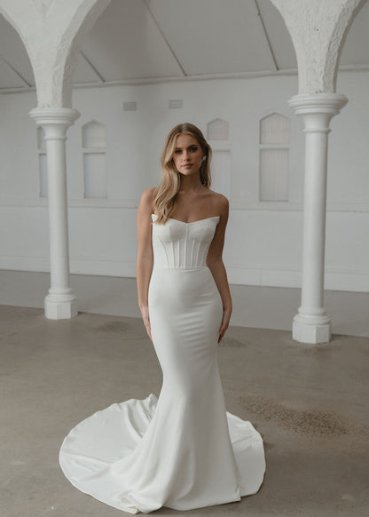 Woman in a white strapless gown standing in an elegant indoor setting with columns.