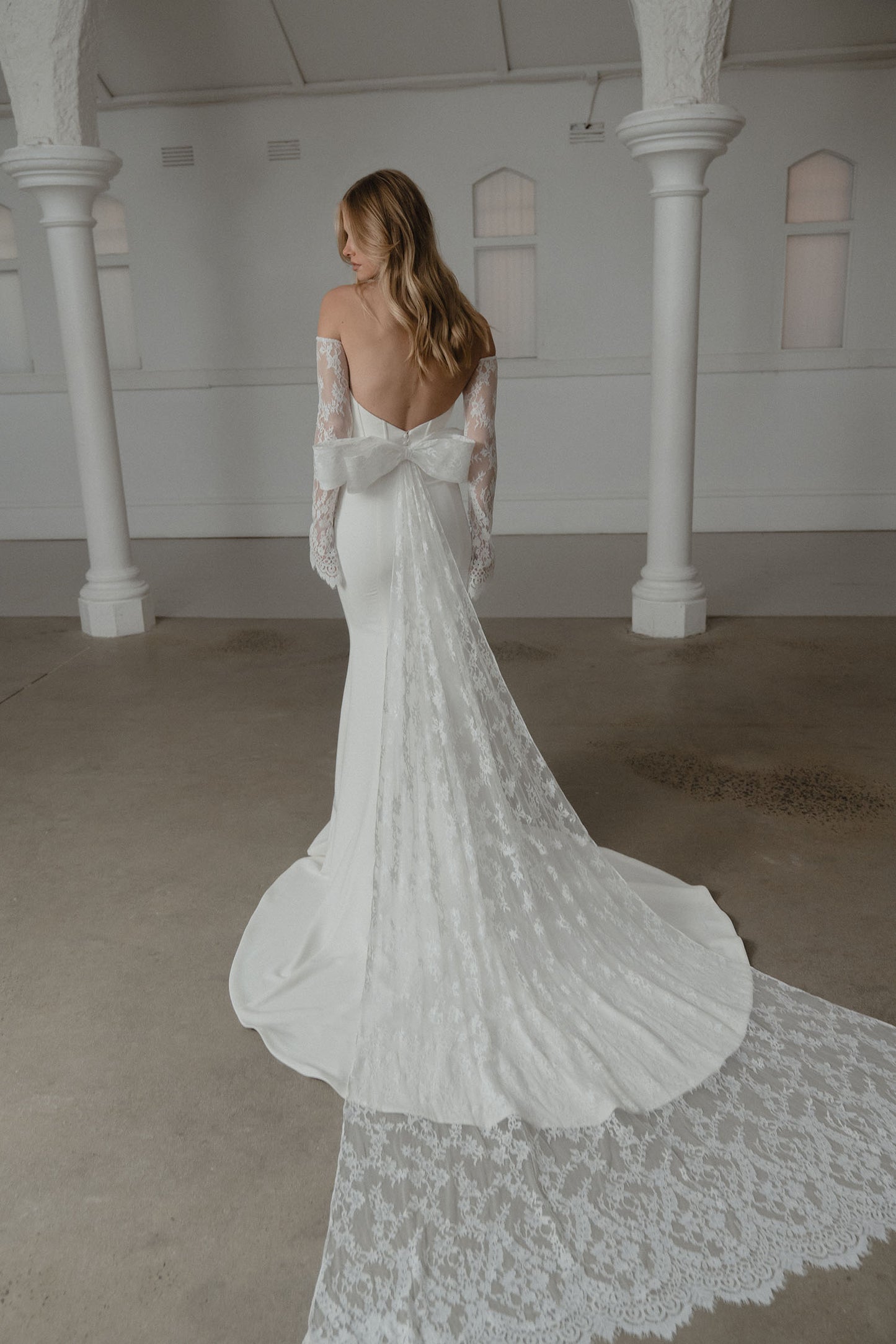 Woman in a white lace wedding dress standing in a room with white columns.