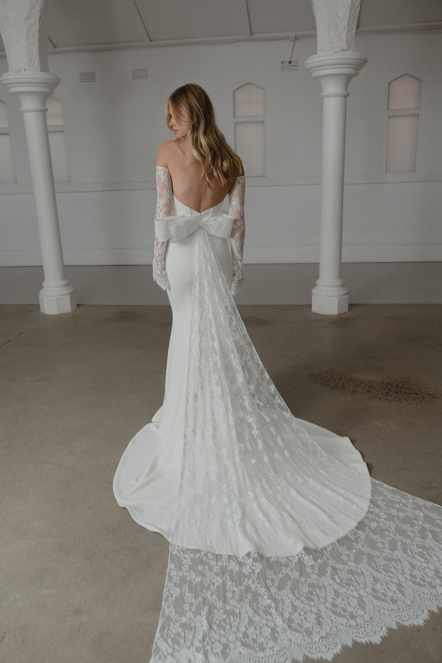 Woman in a white lace wedding dress standing in a room with white columns.