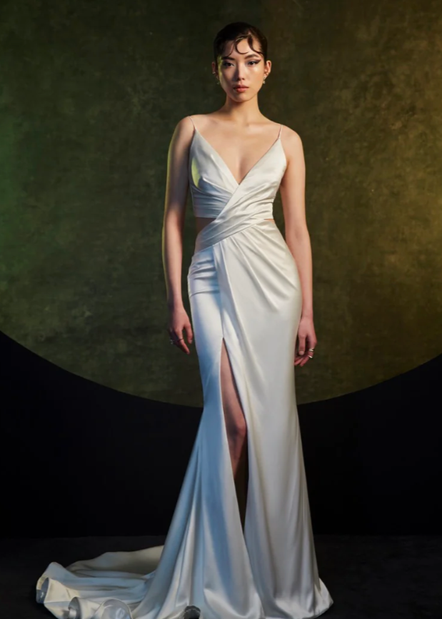 Model wearing Venus by Theia Couture - a fitted v-neck wedding dress with a slit, full body front view
