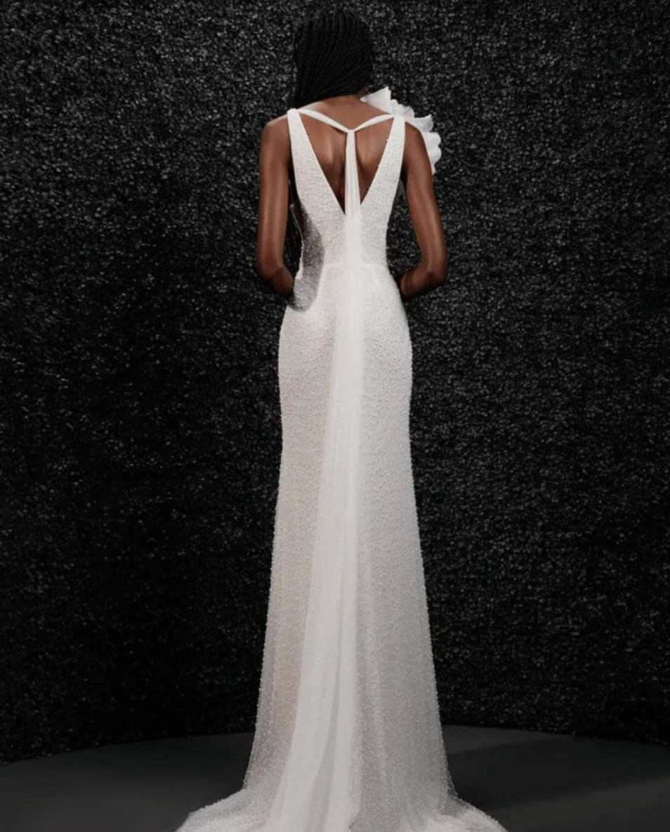 Model wearing Carole by Vera Wang - a fitted beaded wedding dress with a deep V neck and floral shoulder attachment, full body back view