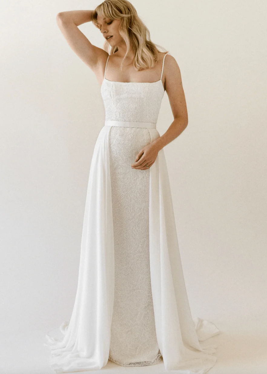 Truvelle Celine is a captivating lace slip gown with a detachable chiffon overskirt! Thin straps highlight the square neckline, while a soft train accents the column skirt. Peony-embroidered beaded lace with dazzling sequins crafts the slim silhouette of the gown.