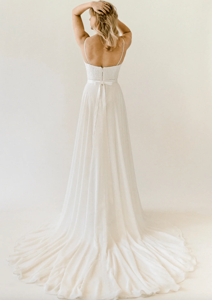 Truvelle Celine is a captivating lace slip gown with a detachable chiffon overskirt! Thin straps highlight the square neckline, while a soft train accents the column skirt. Peony-embroidered beaded lace with dazzling sequins crafts the slim silhouette of the gown.
