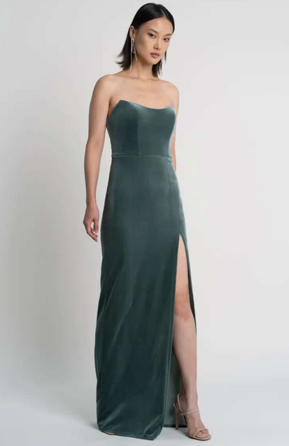 Woman wearing a strapless green gown with a high slit on a white background