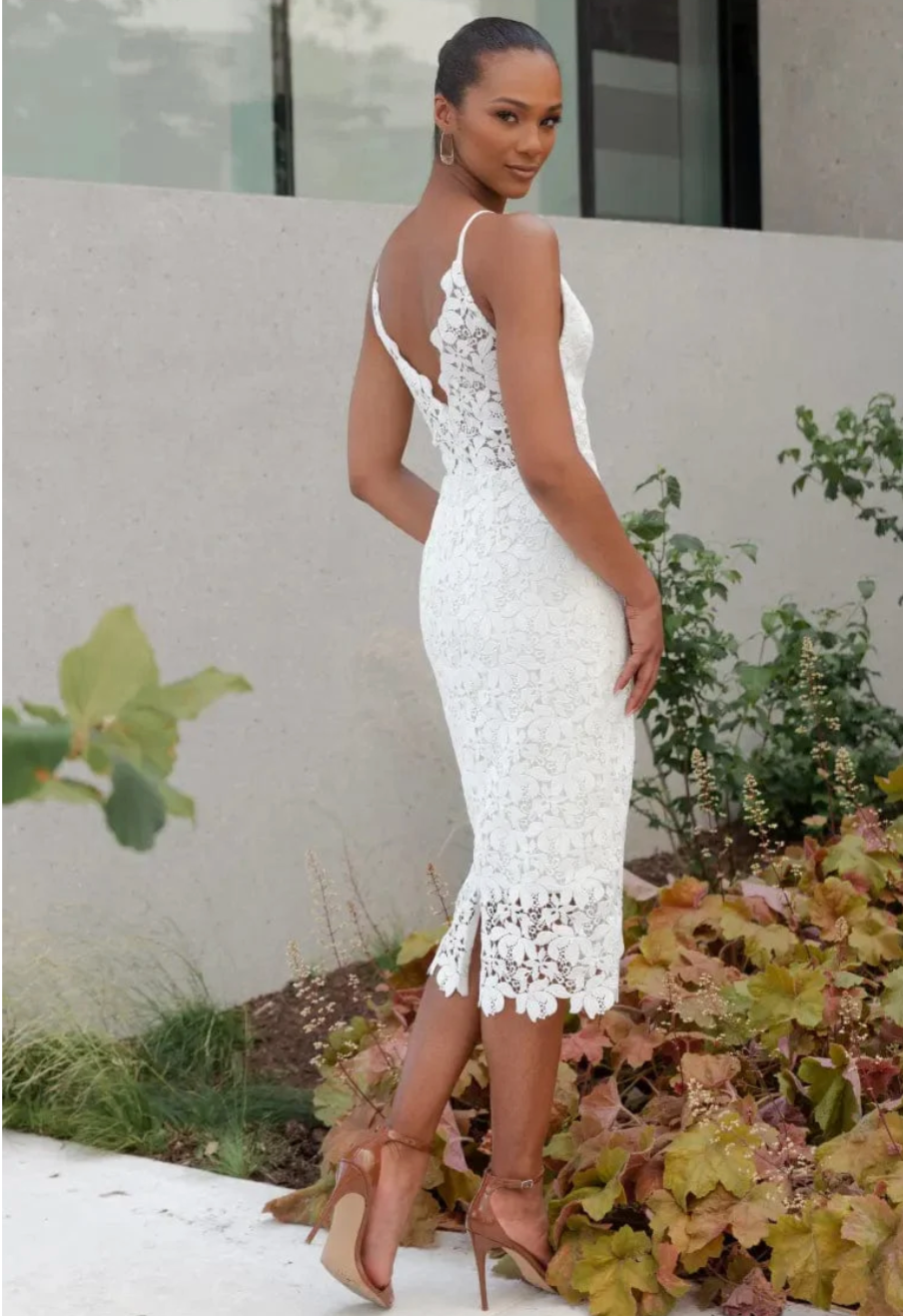Woman wearing a white lace dress standing outdoors with greenery in the background