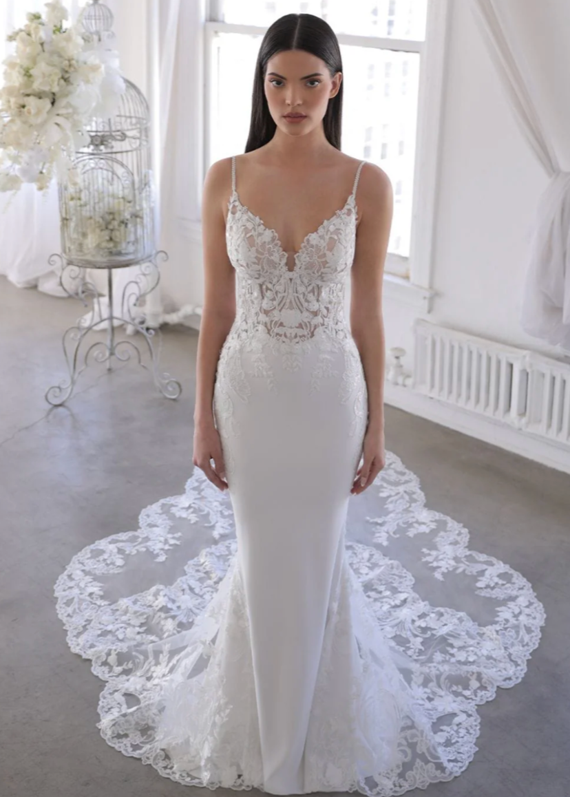 Woman wearing a white lace wedding dress in a bright room with flowers and a birdcage.