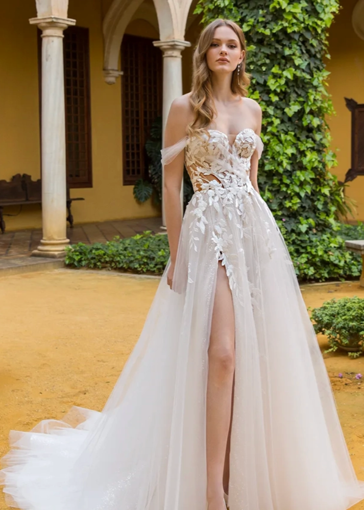 Woman in a white wedding dress with floral details standing in an outdoor setting.