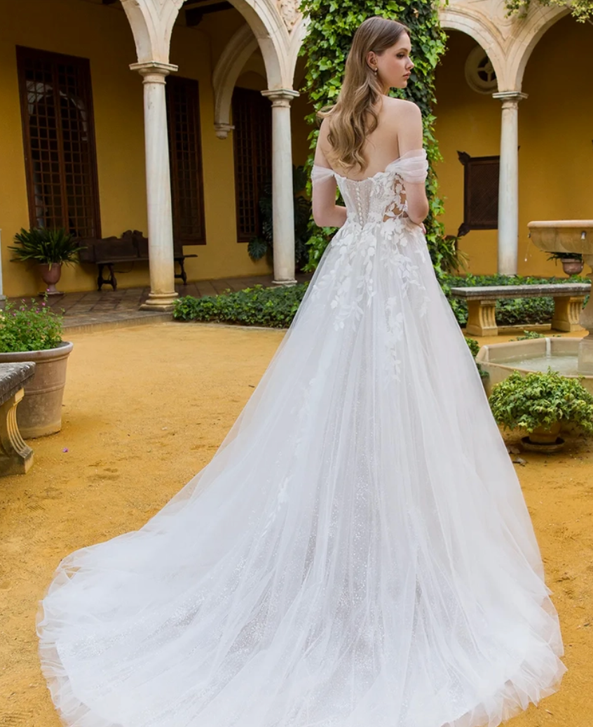 Woman in a white wedding dress standing in an outdoor courtyard with columns and plants.