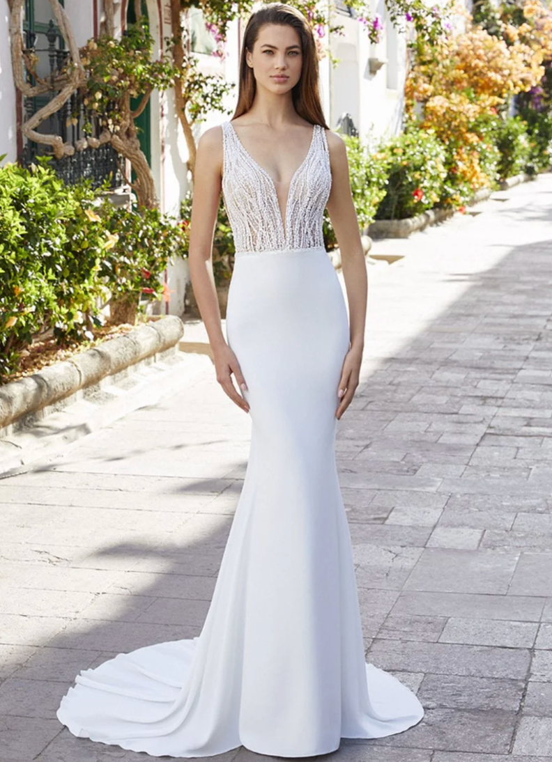 Woman in a white evening gown with lace top standing on a sunlit street.