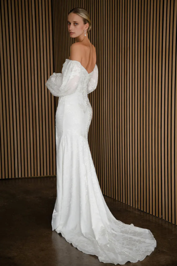 Woman wearing a white wedding dress with a long train against a striped wall.