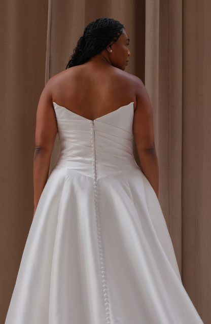 Woman wearing a white strapless wedding dress against a beige curtain background