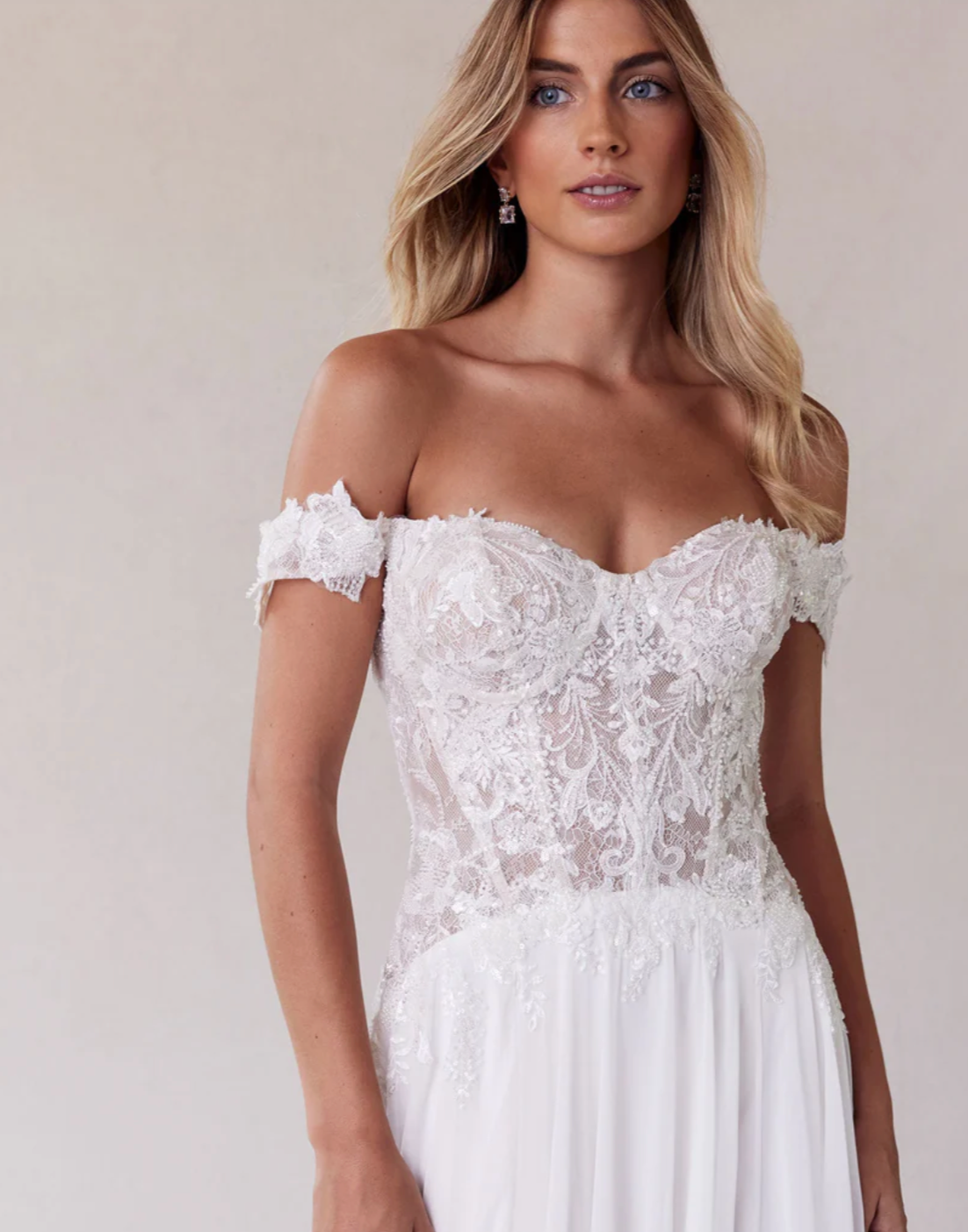 Woman wearing a white lace off-shoulder dress against a plain background