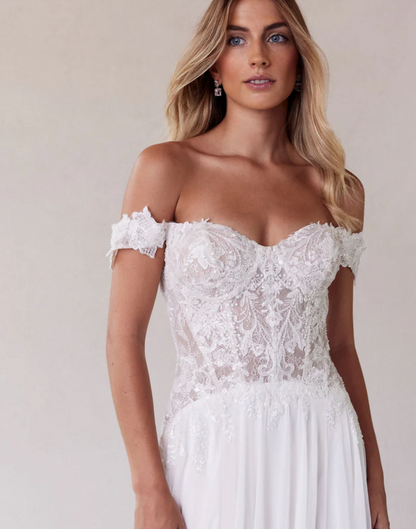 Woman wearing a white lace off-shoulder dress against a plain background