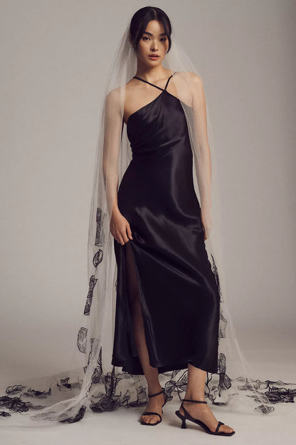 Woman wearing a black satin dress with a sheer veil against a gray background