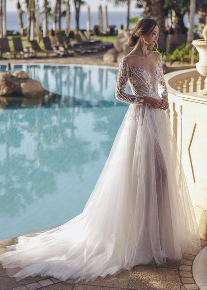 This geometric beaded lace A-line gown is a vision of bridal beauty, and its illusion long sleeves with beaded leafy lace give a mystical, enchanting vibe. The figure-flattering illusion lace bodice hugs the curves, while the flared glitter tulle and soft tulle skirt creates a sense of drama and romance, ensuring you make a lasting impression on your wedding day.