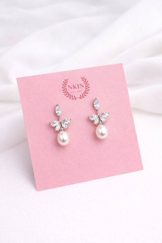 Pearl earrings with minimalist butterfly designs on a pink card with 'NKIN' branding.