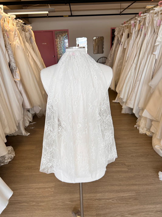 White lace wedding dress on a mannequin in a storage room with folded fabric.
