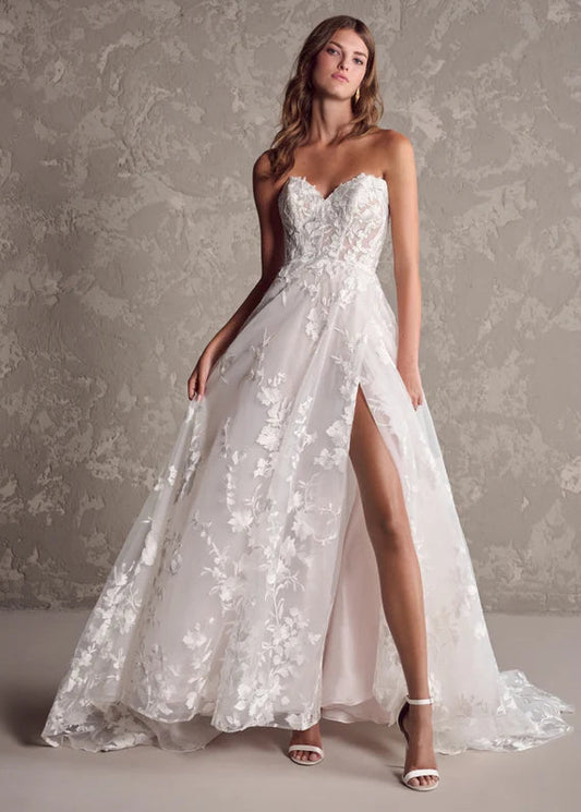 Model wearing a strapless white lace wedding dress with a slit on a textured gray background