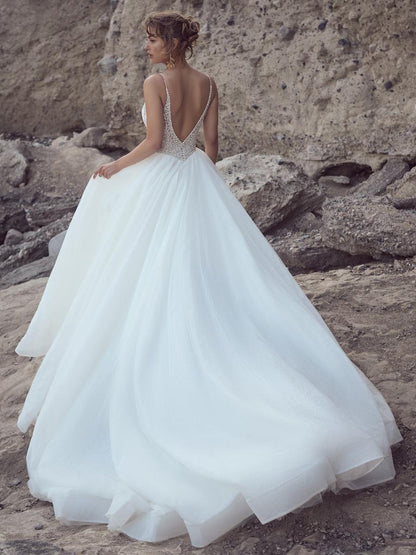 Woman in a white wedding dress with a open back standing on a rocky beach.