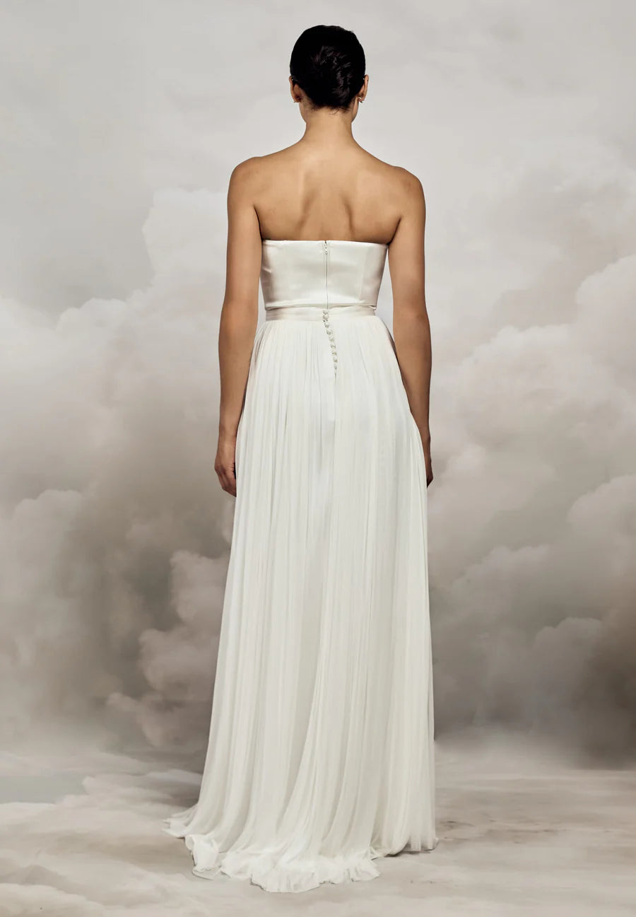 Woman wearing a strapless white wedding dress against a cloudy sky background