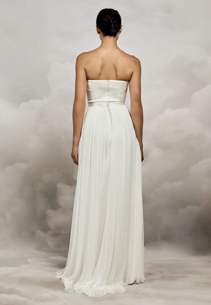 Woman wearing a strapless white wedding dress against a cloudy sky background