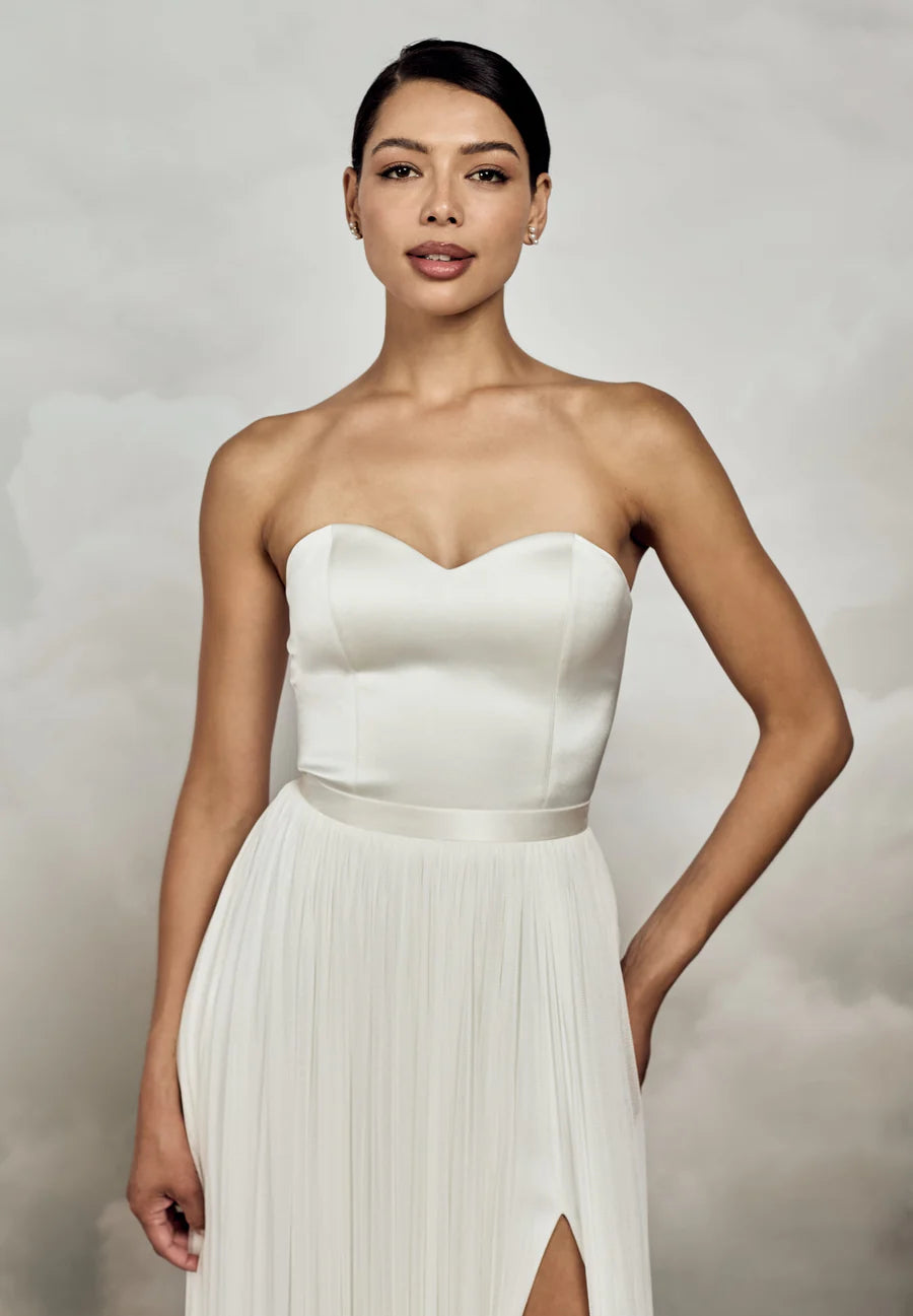 Woman wearing a strapless white gown with a pleated skirt against a neutral background