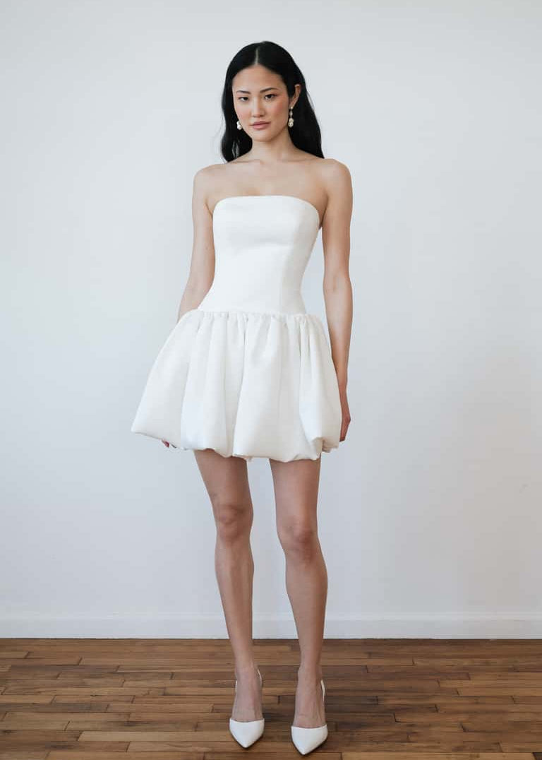 Woman wearing a white strapless dress standing against a plain background
