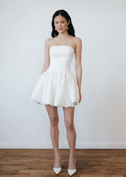 Woman wearing a white strapless dress standing against a plain background