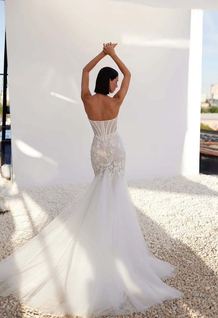 A mermaid silhouette dress in lightskin color made of embroidered lace will help the bride create a seductive image that excites the imagination and causes admiration. A translucent corset with a heart-shaped cutout will emphasize the gorgeous bust. And the lace decor will help to make the waist visually even narrower, covering the structural lines with a decorative strip and draping with a mesh in the form of diagonal small pleats. The top is also delicately decorated with embroidered appliqués.