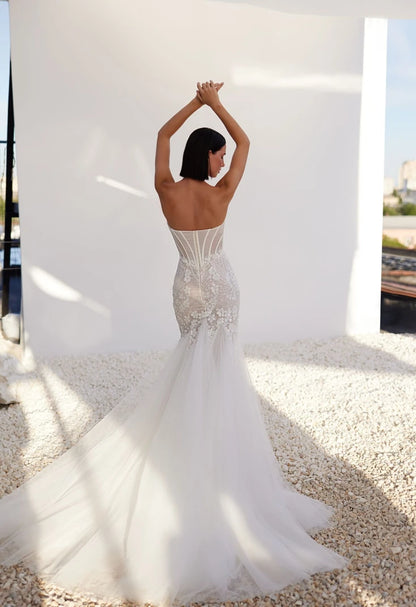 A mermaid silhouette dress in lightskin color made of embroidered lace will help the bride create a seductive image that excites the imagination and causes admiration. A translucent corset with a heart-shaped cutout will emphasize the gorgeous bust. And the lace decor will help to make the waist visually even narrower, covering the structural lines with a decorative strip and draping with a mesh in the form of diagonal small pleats. The top is also delicately decorated with embroidered appliqués.