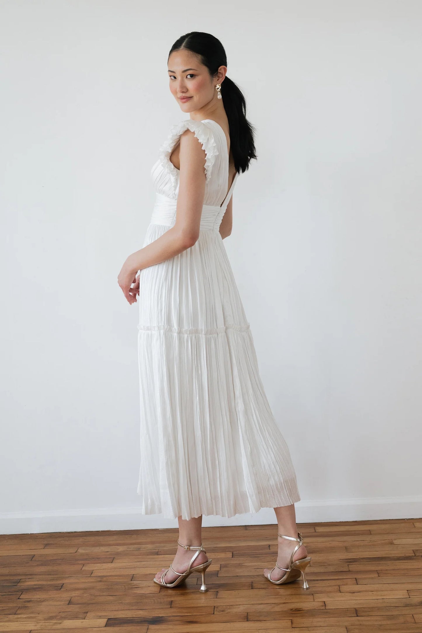 Woman wearing a white dress with cut-out shoulders and pleated skirt on a plain background