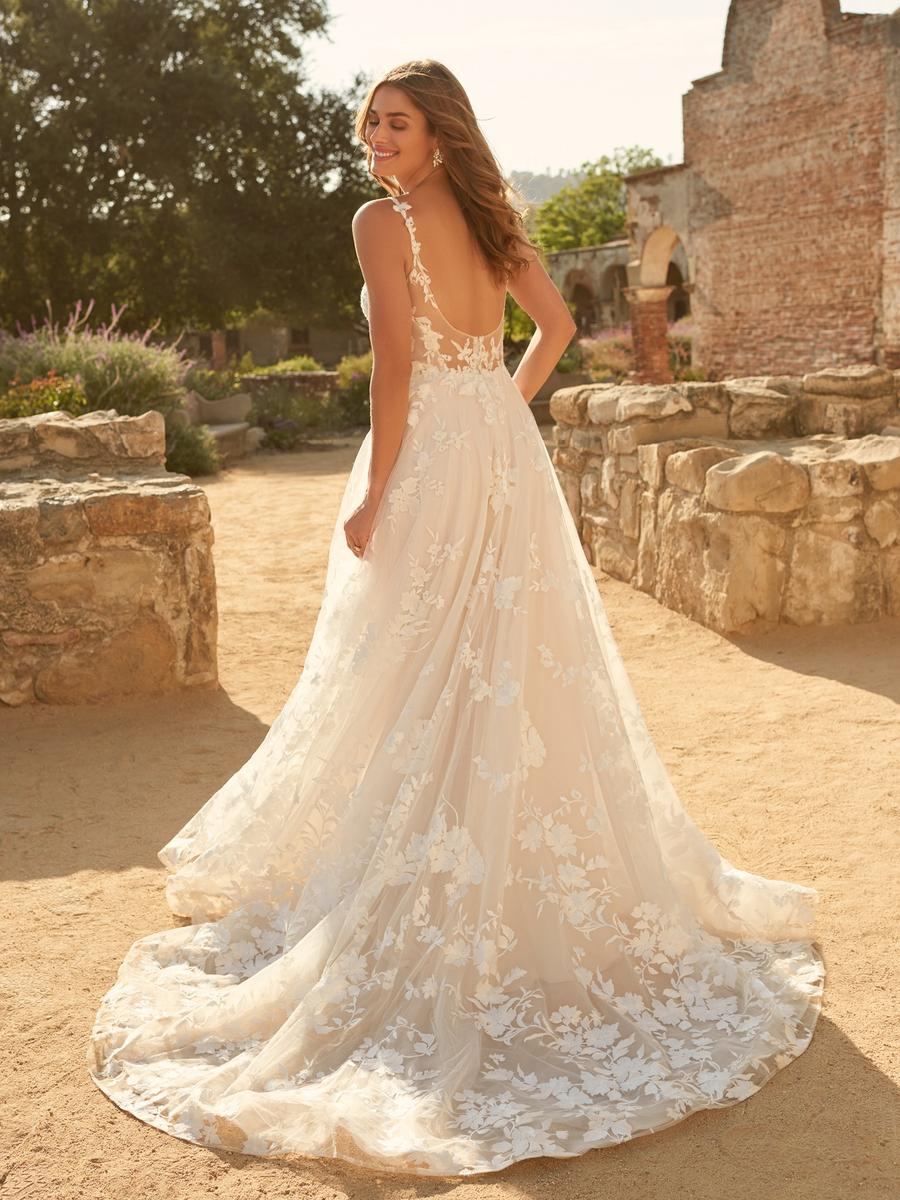 Woman in a white lace wedding dress standing in a rustic outdoor setting.