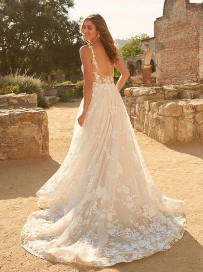 Woman in a white lace wedding dress standing in a rustic outdoor setting.