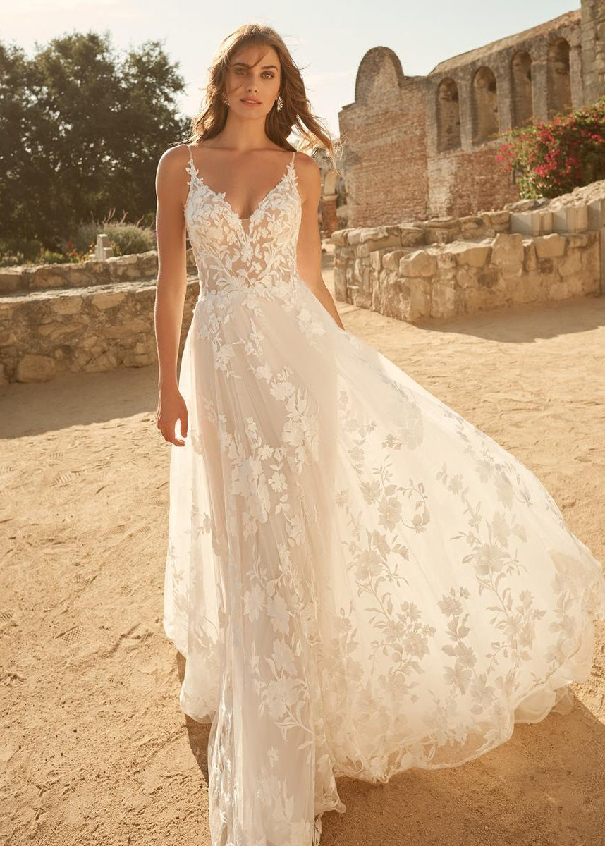 Woman in a white lace wedding dress standing in a sunlit outdoor setting with stone ruins.