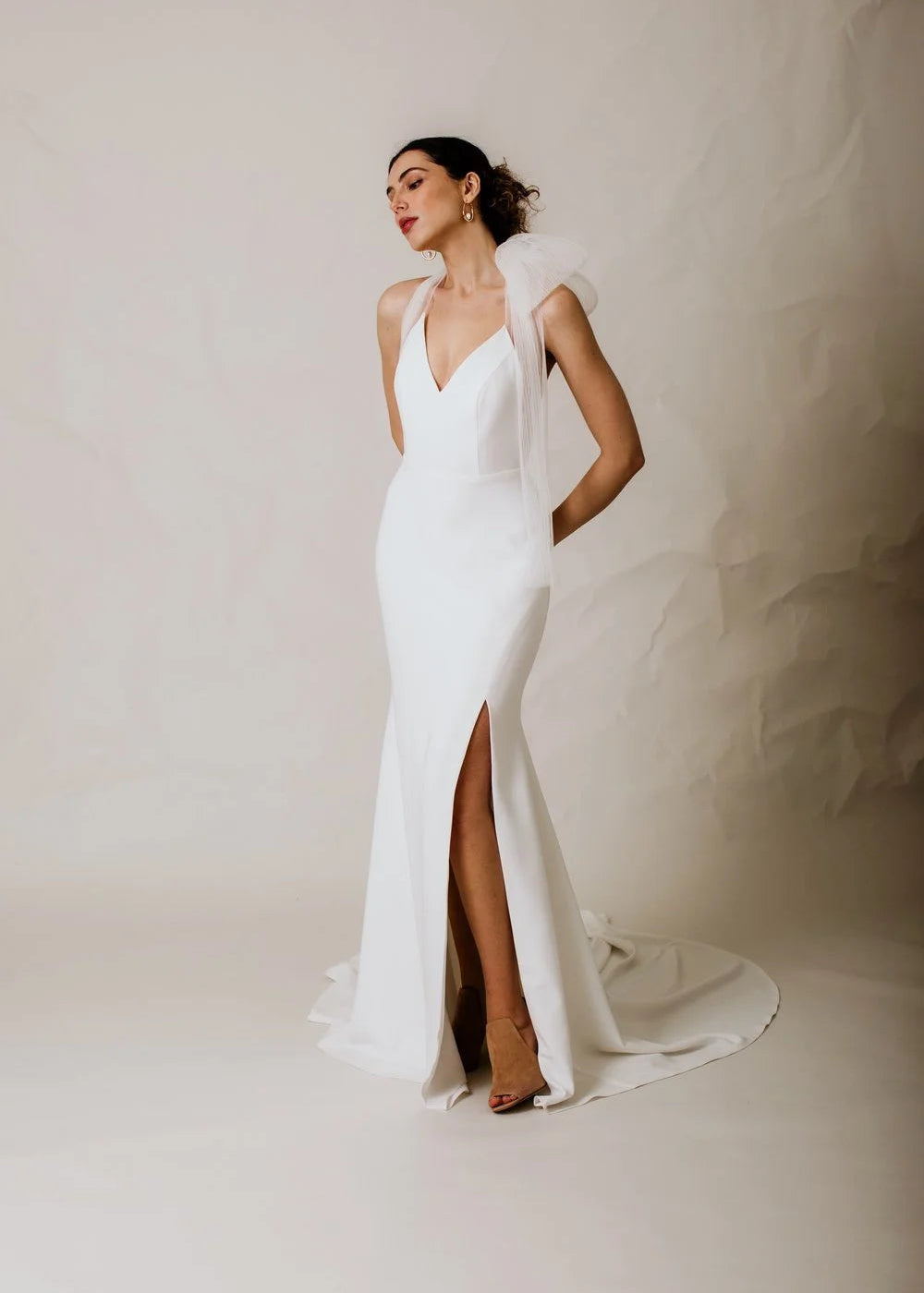 Woman wearing a white wedding dress with a high slit on a plain background