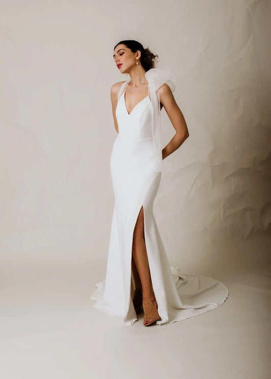 Woman wearing a white wedding dress with a high slit on a plain background