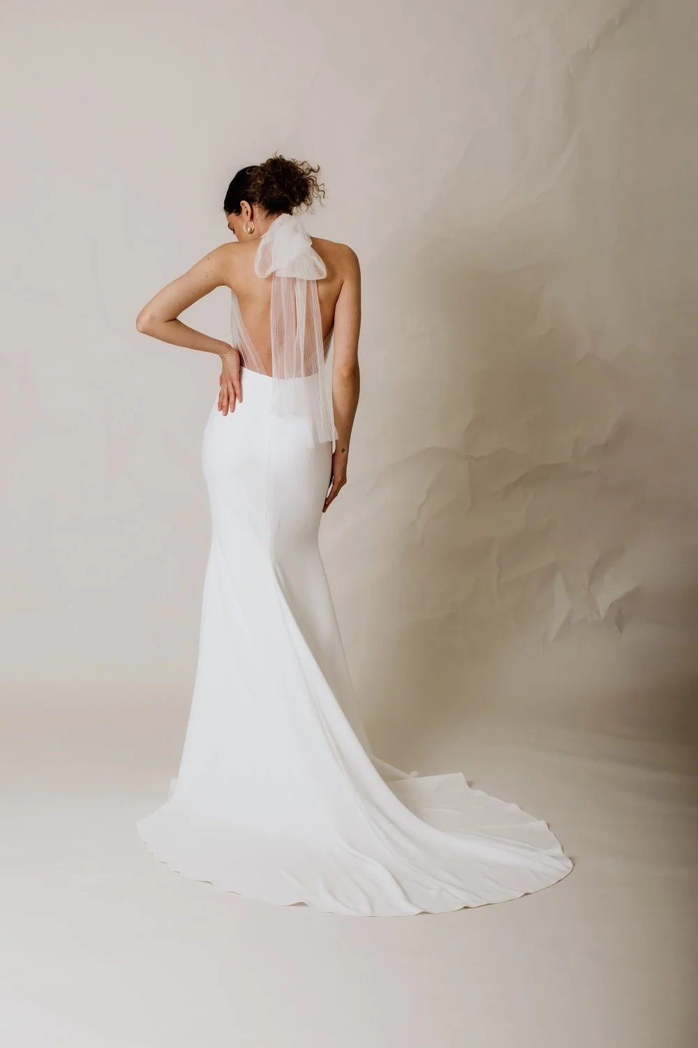 Woman wearing a white wedding dress with a sheer back detail on a plain background