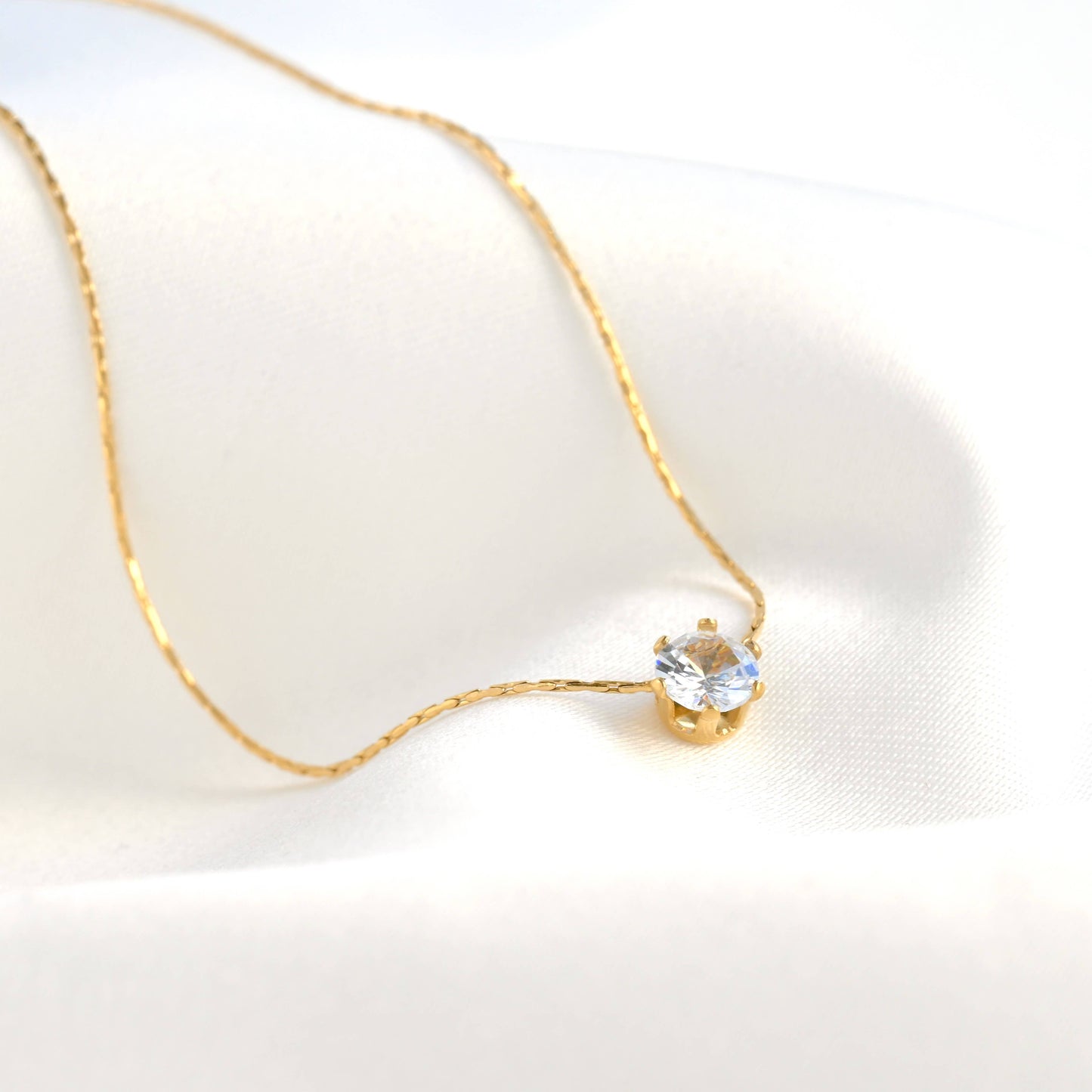 Solitaire necklace with a crystal diamond on a white linen background