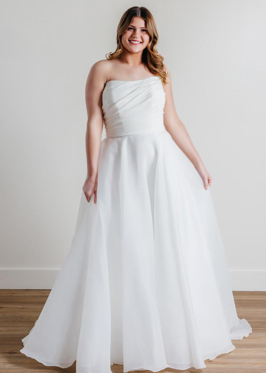 Introducing Fortune, the epitome of elegance and sophistication in bridal fashion. This exquisite wedding dress boasts a timeless strapless design, crafted with meticulous attention to detail. Its luxurious blend of Cyrus Stretch Crepe and Sluler Satin Organza fabrics creates a breathtaking A-line silhouette that will make any bride feel like a true vision of romance on her special day. 