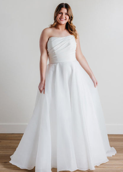 Introducing Fortune, the epitome of elegance and sophistication in bridal fashion. This exquisite wedding dress boasts a timeless strapless design, crafted with meticulous attention to detail. Its luxurious blend of Cyrus Stretch Crepe and Sluler Satin Organza fabrics creates a breathtaking A-line silhouette that will make any bride feel like a true vision of romance on her special day. 